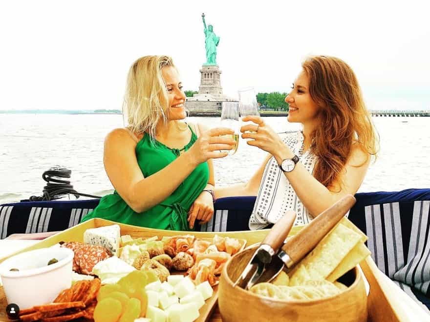 two women making a toast with champagne by the Statue of Liberty during a private boat dinner NYC