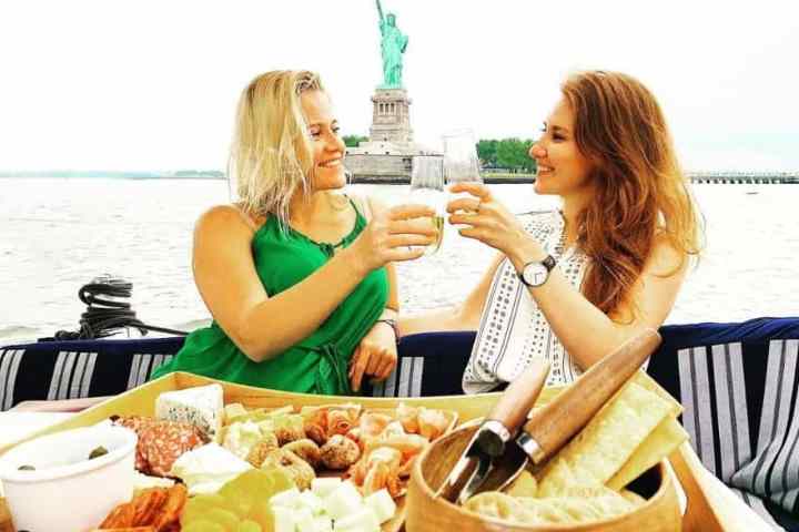 two women making a toast with champagne by the Statue of Liberty during a private boat dinner NYC