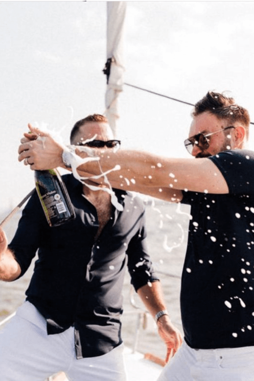 2 men in black shirts popping a champagne bottle during a small party boat rental in NYC